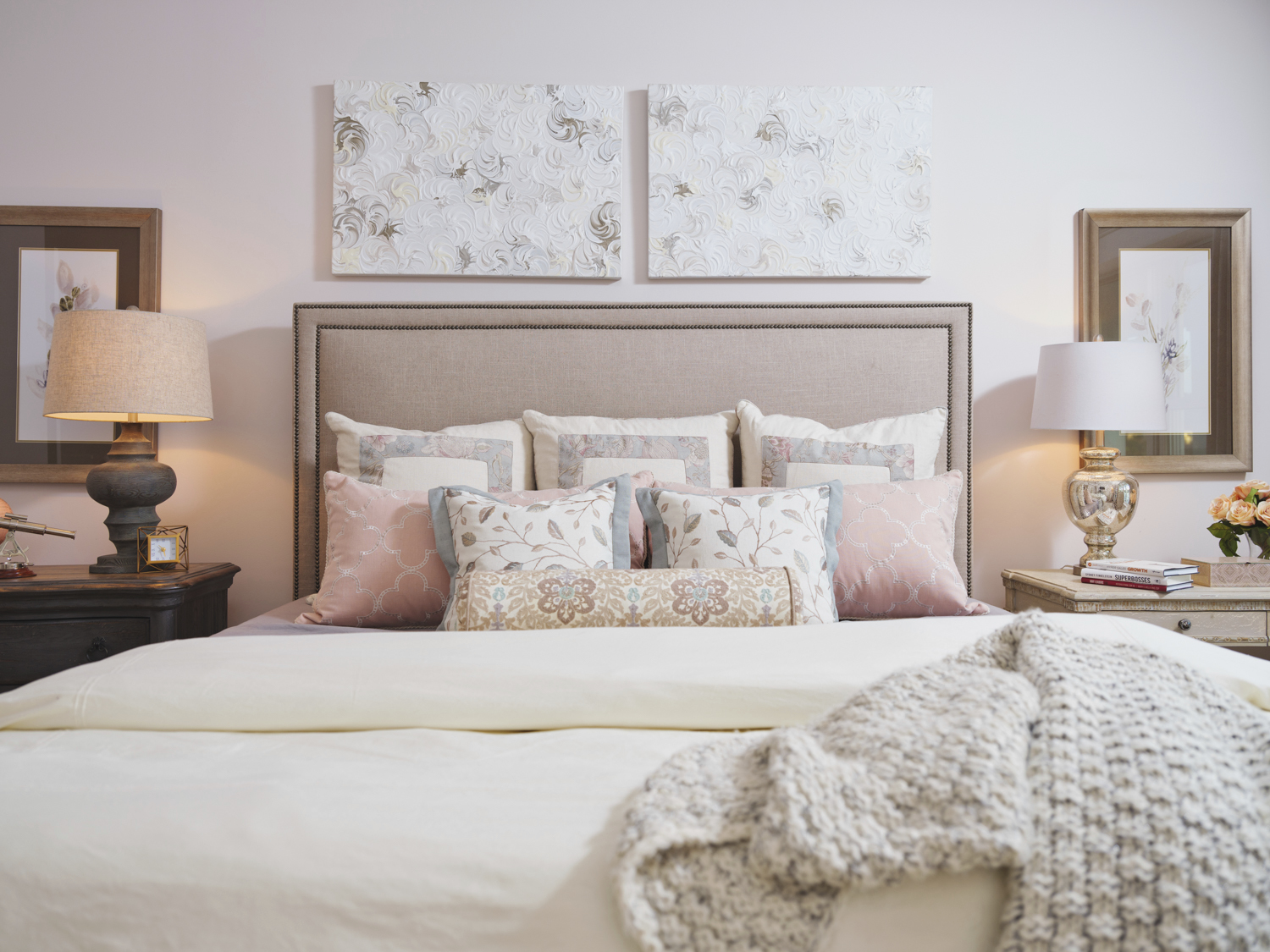 Transforming your bedroom into a cozy retreat, a neatly made bed features multiple patterned pillows and a knitted throw. Two lamps on bedside tables provide soft light, while artwork above the headboard completes the inviting atmosphere.